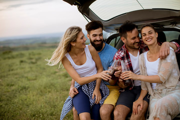 Young people sitting in the car trank during trip in the nature