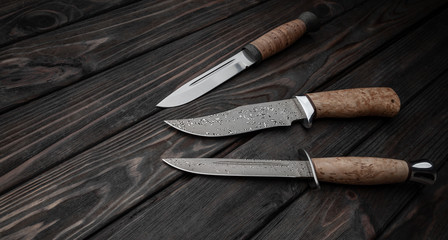 Hunting bowie knife with a wooden handle on dark wooden background. Steel arms weapon. top view
