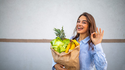 Woman holding a shopping bag full of fresh food. Young woman with a grocery shopping bag. Portrait of beautiful young woman with vegetables in grocery bag.