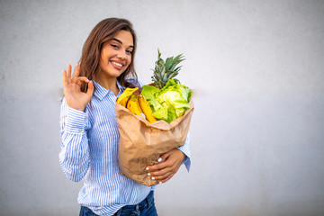 Woman holding a shopping bag full of fresh food. Young woman with a grocery shopping bag. Portrait of beautiful young woman with vegetables in grocery bag.
