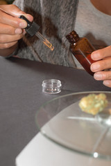 Woman making her own CBD tincture, powerful cannabis extract for pain. Calculating dose of cannabis oil, table with weight and marihuana bud.