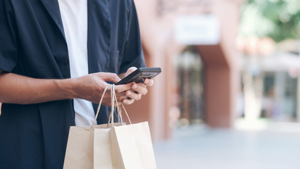 Young man with shopping bags is using a mobile phone while doing shopping