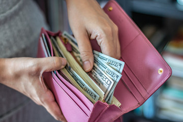 Woman taking out US dollar bills from her pocket wallet (depth of field photography).