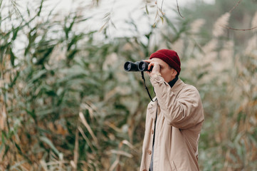 Explorer in forest near lake looks horizon with binoculars