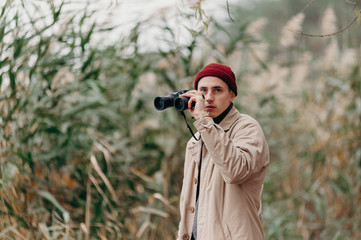 Explorer in forest near lake looks horizon with binoculars