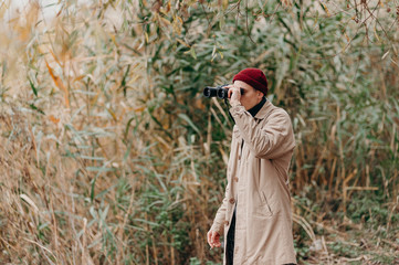 Explorer in forest near lake looks horizon with binoculars