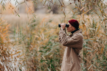 Explorer in forest near lake looks horizon with binoculars