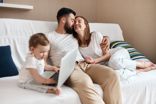 bearded man and beautiful smiling woman sitting on the sofa and hugging while the baby is playing on computer. close up photo