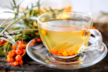 teapot and cup of hot sea buckthorn tea with fresh berries on wooden table