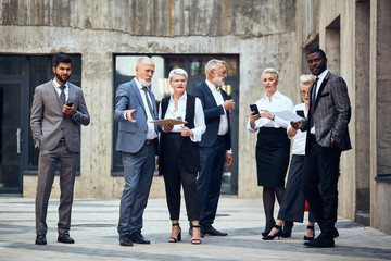 Group of three caucasian men and one african man, three caucasian women wear diferent office wear discuss project outdoor