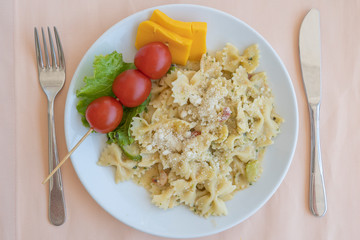 Pasta farfalle with cherry tomato and cheese in white plate, closeup