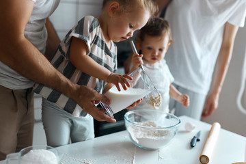 little kids making cream for cake, parents helping them in the kitchen. close up side view photo