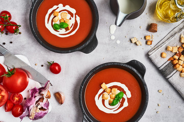 Tomato soup with cream, croutons and basil in a black bowl on stone background. Top view. Copy space for text.