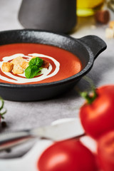 Delicious tomato soup with cream, croutons and basil in a black bowl on stone background. Copy space for text. Selective focus.