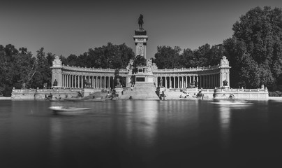 Monochrome long exposure of people on boats across from monument to Alfonso XII in the Parque del Buen Retiro, known as the Park of the Pleasant Retreat in Madrid, Spain
