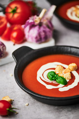 Delicious tomato soup with cream, croutons and basil in a black bowl on stone background. Copy space for text. Selective focus.