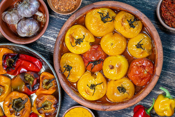 Baked red and yellow tomato and bell pepper. Tomatoes and bell peppers in a baking dish on a wooden table. A healthy and delicious vegetarian dish. Closeup, top view