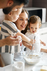 smiling positive woman standing between her daughters looking aside while cooking dough