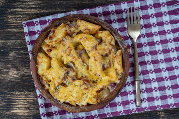 Baked potato, onion and garlic with cheese on the wooden table, close up. Ceramic bowl with potato onion and garlic slices background