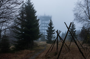 Barbwire fence. Part of the czech german borderline in the middle of a foest on a grey and foggy autumn morning. Trail leading towards an old rotten military boarder watchtower