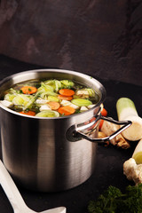 Broth with carrots, onions various fresh vegetables in a pot - colorful fresh clear spring soup. Rural kitchen scenery vegetarian broth