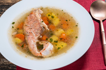 Fresh salmon fish soup with carrots and potatoes in a white plate, close up