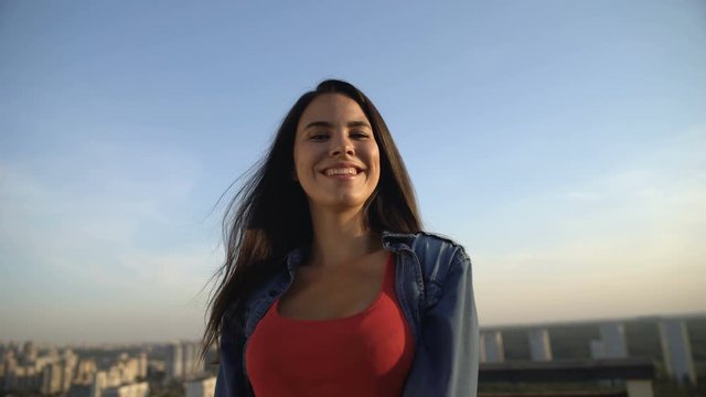 Smiling female model posing at camera on roof top, photo shoot, city view