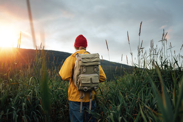 Back view of man tourist with backpack standing in front of the mountain massif while journey by scandinavian. Male traveler wearing yellow jacket explore national park and hiking outdoor landscape
