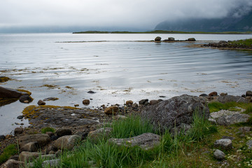 Beautiful nature landscape in North. Scenic outdoors view. Ocean with waves and mountains. Big dark stones. Dramatic storm clouds. Extreme weather, rain and wind. Explore Norway, summer adventure