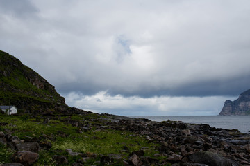 Beautiful nature landscape in North. Scenic outdoors view. Ocean with waves and mountains. Big dark stones. Dramatic storm clouds. Extreme weather, rain and wind. Explore Norway, summer adventure