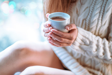 Comforting cozy woman in knitted winter white warm sweater resting and warming up with a cup of hot...