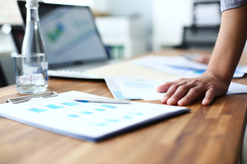 Male hands on the office desk. Young businessman holding a pen in hand and studies the results of sales represented on the graphics. Concept of office workplace.