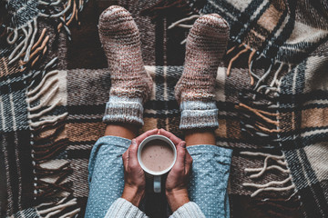 Cozy woman in knitted winter warm socks and in pajamas holding a cup of hot cocoa during resting on...
