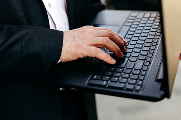 Cropping image of senior businessman holding laptop in his hand and typing closeup.- Image