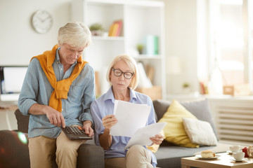 Portrait of modern senior couple calculating finances and budget while preparing tax report at...