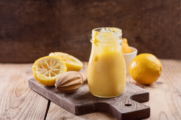 Lemon curd in a glass jar on a wooden background, ingredients for cooking, lemon kyrd recipe