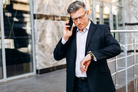 Business, punctuality and people concept - senior businessman checking time on watch on his hand in city