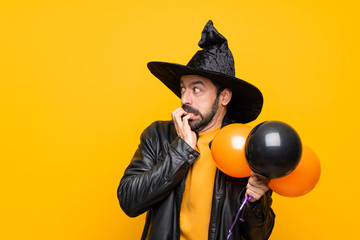 Man with witch hat holding black and orange air balloons for halloween party nervous and scared...