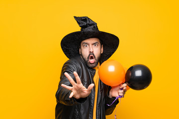 Man with witch hat holding black and orange air balloons for halloween party nervous stretching hands to the front