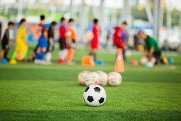 Fototapeta premium Soccer ball on green artificial turf with blurry soccer team training. Blurry kid player training and soccer equipment in soccer academy.