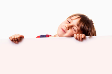 Funny portrait of cute sleepy little child girl behind white empty banner. Free space for text.