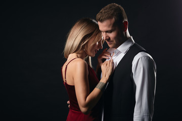 sexy young couple dancing erotic dance, blonde woman in red dress helping guy to take off his shirt. close up portrait, isolated black background, studio shot.