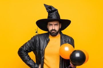 Man with witch hat holding black and orange air balloons for halloween party angry