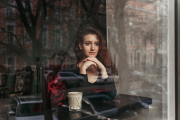 Fototapeta na wymiar Beautiful brunette with long hair in a cafe behind a glass, portrait