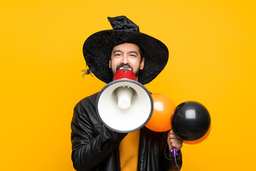 Man with witch hat holding black and orange air balloons for halloween party shouting through a megaphone