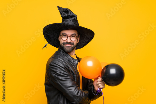 Man with witch hat holding black and orange air balloons for halloween party with glasses and smiling