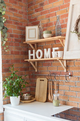 Modern kitchen in loft style, brick wall, shelfs, word HOME, and plant. Interior details