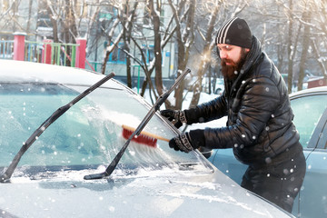 man cleans snow from the glass at the car