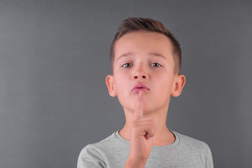 Handsome brunette boy showed with finger keep silenе over grey background