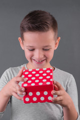 Сheerful brunette boy opens gift box over grey background, concept of children's emotions and holiday